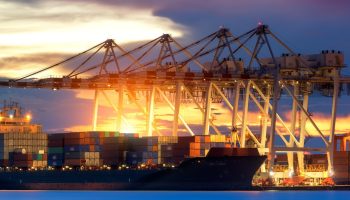 Container Cargo freight ship with working crane bridge in shipyard at dusk for Logistic Import Export background